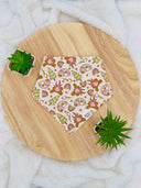 Overhead view of a pet bandana with a pink camping-themed print featuring campers, trees, campfires, rainbows, and marshmallows roasting on sticks. The bandana is neatly laid out, highlighting the fun, adventurous design.